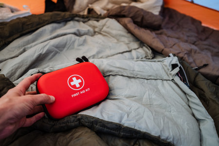 A hand extends a small red first aid kit placed on a cozy jacket, perfect for adventurous individuals who prioritize safety and preparedness while enjoying their outdoor activities and explorationsの写真素材