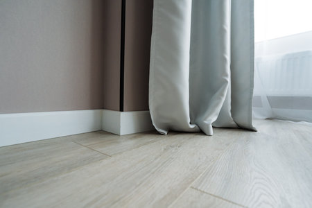 In a charming interior, elegant white curtains cascade onto polished wood floor by a bright window, allowing sunlight to flood the room with a warm glow, enhancing the overall atmosphereの写真素材