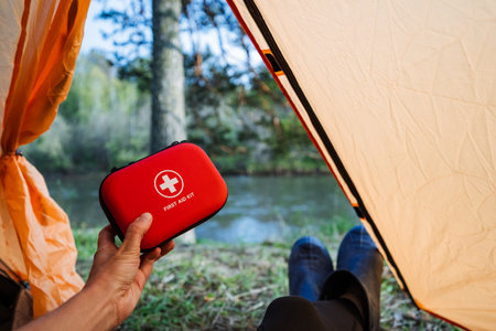 In a cozy tent, a hand grips a compact red first aid kit, perfectly placed in nature, making it an ideal companion for outdoor enthusiasts, ensuring everyones safety on camping adventuresの写真素材
