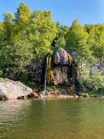 In the center of a serene lake, there exists a beautiful waterfall, which cascades gracefully down into the water, and this enchanting scene is further enhanced by the lush trees surrounding itの写真素材