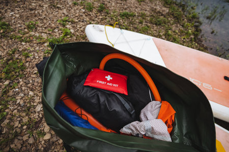 Explore musthave items for a fun day on the water, shown in this image with a waterproof bag of gear, clothing, and a first aid kit next to a paddleboard for a safe outdoor adventureの写真素材