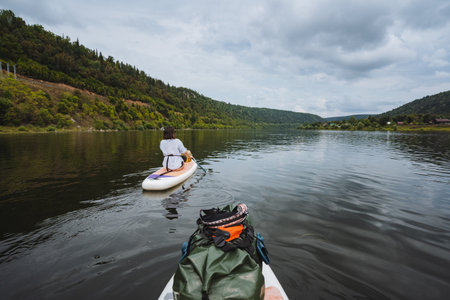 Experience a serene paddleboarding journey on a calm river, surrounded by stunning hills and lush greenery perfect for nature lovers seeking tranquility, relaxation, and the beauty of the outdoorsの写真素材