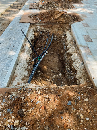 A freshly dug trench reveals exposed cables and displaced soil, clearly indicating that ongoing utility installation is taking place in a construction area that has been marked for new developmentsの写真素材