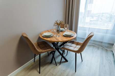 In a cozy living room, a charming wooden table is surrounded by comfortable chairs near a large window that enhances natural light, creating an inviting and warm atmosphere for all who gatherの写真素材