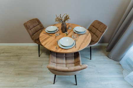 A beautifully crafted wooden table is arranged with colorful plates, shiny utensils, and a vase of fresh flowers, creating an elegant display that enhances the room's aesthetics and invites warmthの写真素材