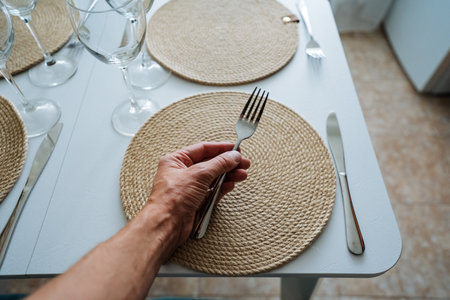 An individual proudly holds a sparkling fork before a meticulously arranged dining table with an elegant placemat, creating a warm and inviting atmosphere for enjoying a meal with loved onesの写真素材