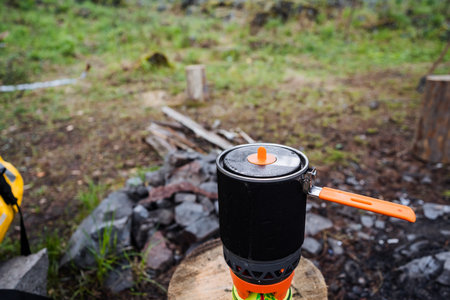 A portable camping stove rests on a sturdy, resilient stump in a breathtaking wilderness area that features a cozy campfire spot surrounded by vibrant, lush greenery and captivating landscapesの写真素材