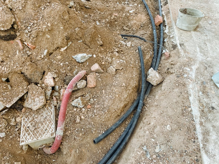 A chaotic assortment of various wires and cables lies haphazardly in the dirt, intertwining and creating an unkempt appearance that is scattered across the ground, forming a cluttered sceneの写真素材