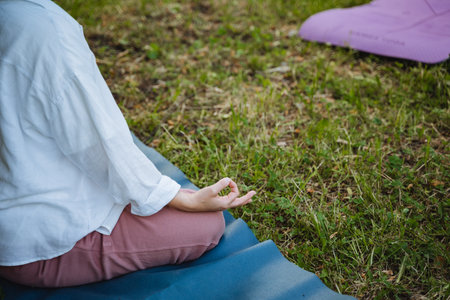 In a serene and peaceful scene, an individual is peacefully meditating on a colorful yoga mat, surrounded by a lush green outdoor setting, embodying tranquility and mindfulness in harmony with natureの写真素材