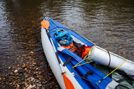 A colorful kayak rests on a rocky shore by the calm waters, packed with outdoor gear, including a sleeping bag, ready for a peaceful day of exploration and funの写真素材