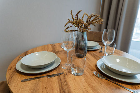 A beautifully crafted wooden table that is set with elegant plates, shiny glasses, and a lovely vase...
