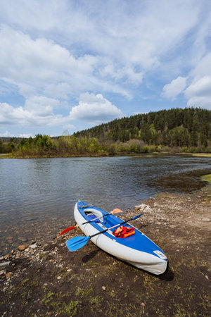 A colorful kayak sits on the riverbank, surrounded by lush greenery and a wideopen sky, offering a serene spot for outdoor enthusiasts to explore nature and find tranquility away from daily lifeの写真素材