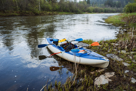 A vibrant blue kayak rests peacefully on the riverbank, surrounded by lush greenery and calm waters, capturing the essence of outdoor adventure, joy, and tranquility in natures embraceの写真素材