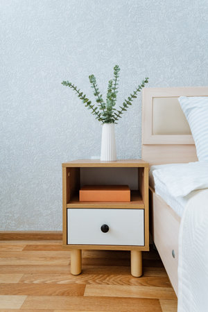 A beautifully designed nightstand that features a lovely vase of fresh flowers and an interesting book resting on it, situated right next to a comfortable bed, creating an inviting atmosphereの写真素材