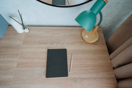 A polished wooden desk is the centerpiece of this workspace, featuring a stylish lamp and a casually placed notebook, creating a warm, inviting atmosphere that enhances productivityの写真素材