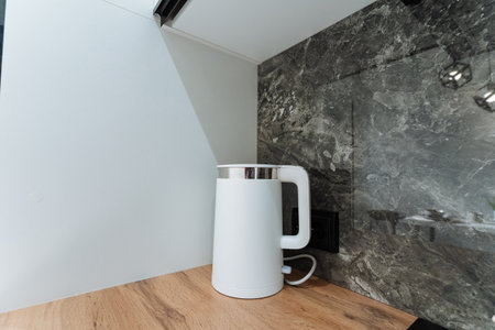 A sleek white electric kettle is elegantly placed on a warm wooden countertop, contrasting beautifully with a stylish marble wall, showing a modern kitchen design ideal for contemporary livingの写真素材