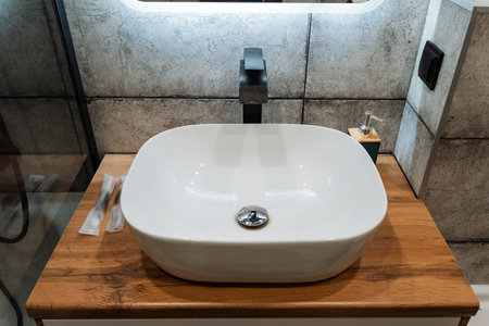 This modern bathroom features a sleek white vessel sink on a warm wooden countertop, complemented by...