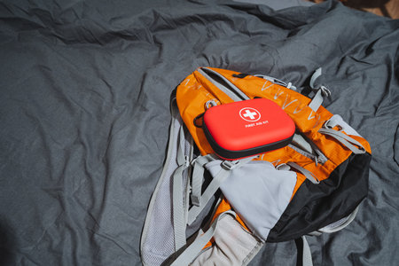 A bright orange backpack and a bold red carrying case rest on a light gray bedspread, highlighting...
