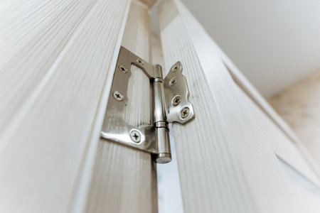 This is a view of a sleek silver door hinges securely on a stylish light wood cabinet, blending modern design and superb functionality, ideal for home improvement and interior designの写真素材