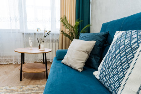 This modern living room features a cozy blue sofa with decorative pillows, a stylish wooden coffee table, and vibrant greenery, enhancing the overall aesthetic of the lively interior designの写真素材