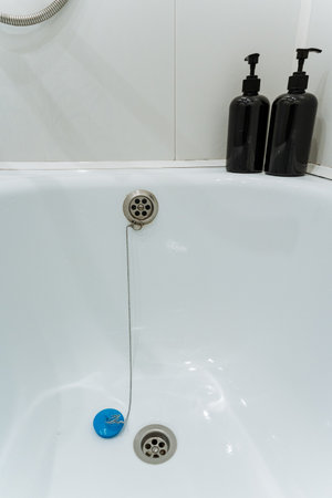 This modern bathroom features a white bathtub with a chic blue drain stopper and stylish black...