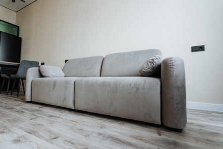 In a modern living room with polished wooden floors and neutral walls, a stylish light beige sofa adds contemporary flair, creating a warm, cozy atmosphere for relaxation and social gatheringsの写真素材