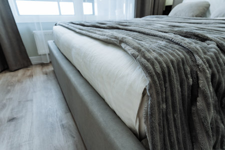 A beautifully styled bedroom showcasing a cozy bed with a soft gray blanket draped elegantly over the edge of the bed, providing a warm and inviting atmosphere that encourages relaxation and comfortの写真素材