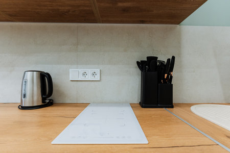 A stylish kitchen countertop features a sleek electric kettle and a modern black utensils holder...