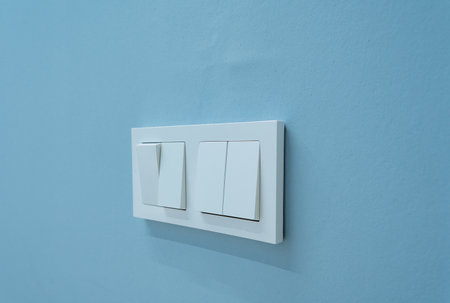 A sleek and modern light switch panel featuring dual switches, set against a calming blue wall. Perfect for contemporary home decor or interior design inspirationの写真素材