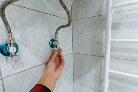 This captivating image shows a closeup of a hand adjusting a quality valve in a modern bathroom with elegant tiles and a cozy heated towel rack, adding luxury and convenience to daily routinesの写真素材