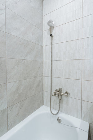 This modern shower includes an elegant handheld showerhead, stylish wall tiles, and a comfortable bathtub, ideal for those wanting a contemporary bathroom design focused on comfort and eleganceの写真素材