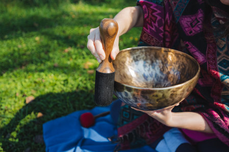In a tranquil outdoor setting, a person is softly playing a Tibetan singing bowl, which fosters relaxation and mindfulness while surrounded by the exquisite beauty of nature all around themの写真素材