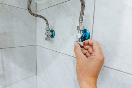 A hand carefully adjusts the water shutoff valve in a modern shower, which showcases the intricate plumbing fixtures and the neatly arranged tiles in a clean, wellmaintained bathroom environmentの写真素材