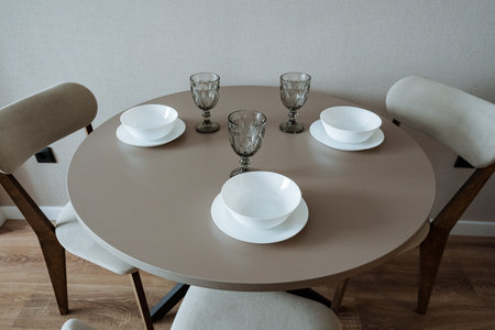 A chic round dining table with elegant white plates and modern glassware creates a welcoming...