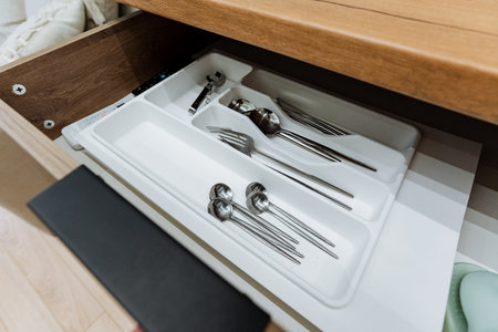 In the kitchen drawer, everything is neatly arranged there is a cutlery holder filled with an...