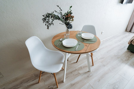 This is a cozy dining space that features a minimalistic round table elegantly adorned with stylish dinnerware and a beautiful fresh floral arrangement, perfect for enhancing modern home aestheticsの写真素材