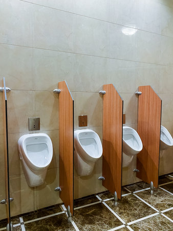 In a public restroom, there is a neatly arranged row of urinals, each separated by wooden dividers...