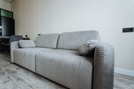 A sleek gray sofa with plush fabric and a contemporary design against a minimalist wall. Ideal for modern interiors, it enhances cozy living spaces while providing comfort and styleの写真素材