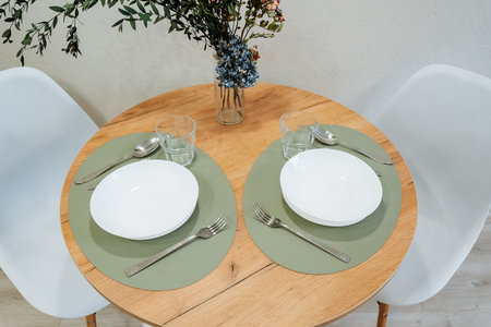 This stylish dining setup features a wooden table, vibrant green placemats, elegant white plates,...