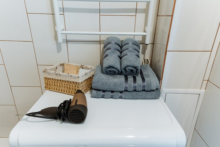 A neatly arranged stack of fluffy towels is sitting on top of a washing machine, which is conveniently positioned next to a hair dryer, creating an organized space for personal grooming and careの写真素材