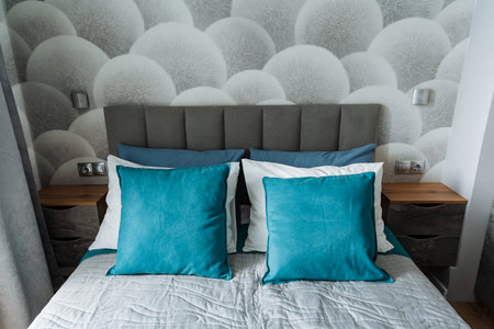 In a modernized bedroom, a cozy bed with plush teal pillows is set against soft gray walls. Elegant wooden nightstands add charm, creating a perfect space for relaxation and comfortの写真素材