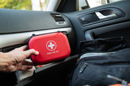 A highly responsible person is diligently organizing a red first aid kit in the cars glove compartment, carefully sorting through items for quick and easy access during potential travel emergenciesの写真素材