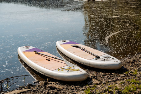 Two vibrant paddleboards rest beside a calm lake, surrounded by lush nature. Its an ideal spot for water sports enthusiasts and nature lovers to relax and enjoy outdoor activitiesの写真素材