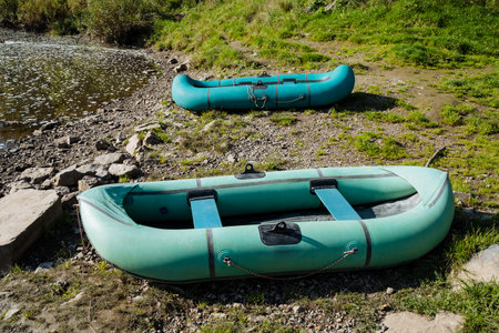 On the sunlit riverbank, two bright green inflatable rafts rest among lush greenery, creating an ideal setting for unforgettable river adventures and peaceful explorations of serene lakesの写真素材
