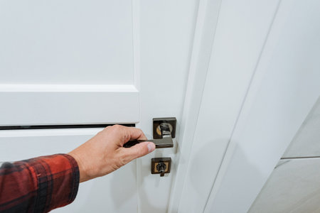 A person is carefully and cautiously opening a sleek white door by turning the polished handle,...