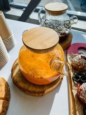A beautifully crafted glass teapot with a natural wooden lid is elegantly positioned on a rustic...