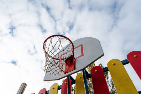 A basketball hoop is perched high above on a vibrant and colorful fence that stands out in the...