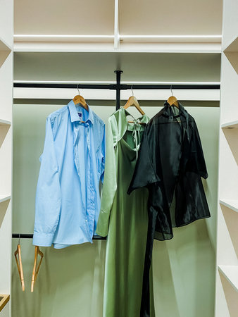 An elegantly designed clothing rack is beautifully showcasing a vibrant blue shirt, a lovely green dress, and a chic black blouse, which are all reflections of the latest contemporary fashion trendsの写真素材