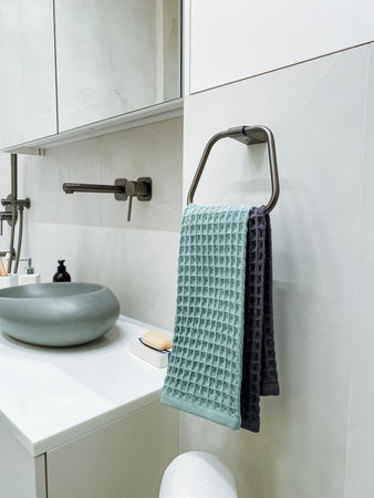 This modern bathroom features a stylish design with a sleek sink, elegantly arranged towels on a stainless steel rack, and minimalistic elements that promote relaxation and comfortの写真素材