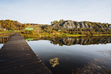 Imagine a serene lakeside view with a wooden dock extending into calm waters, framed by autumn foliage and hillsa perfect spot for nature lovers seeking tranquility away from the hustleの写真素材